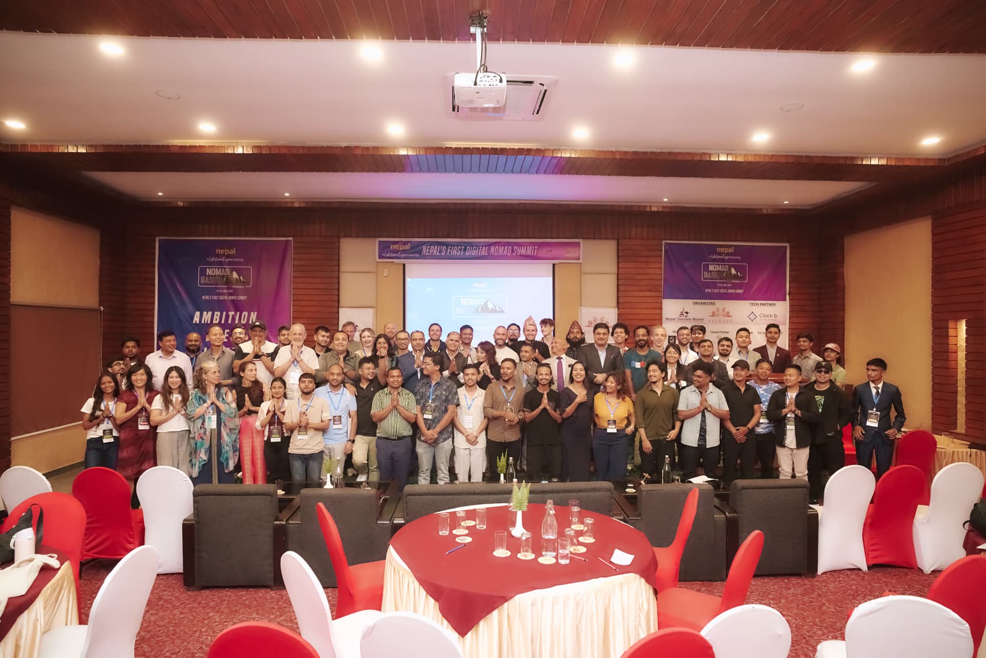 The full Nomads Basecamp 2025 group on stage in Pokhara, beneath the event banner