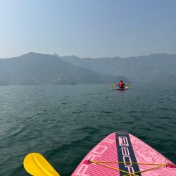 A serene kayaking scene on Phewa Lake in Nepal with distant mountains and clear blue skies.